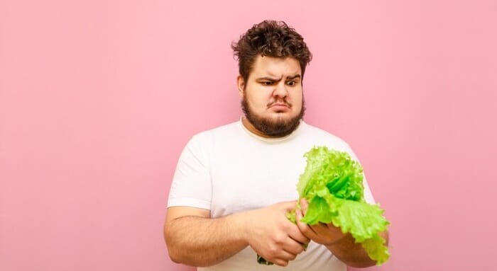 Brodady mężczyzna z nadwagą, patrzący na liście sałaty